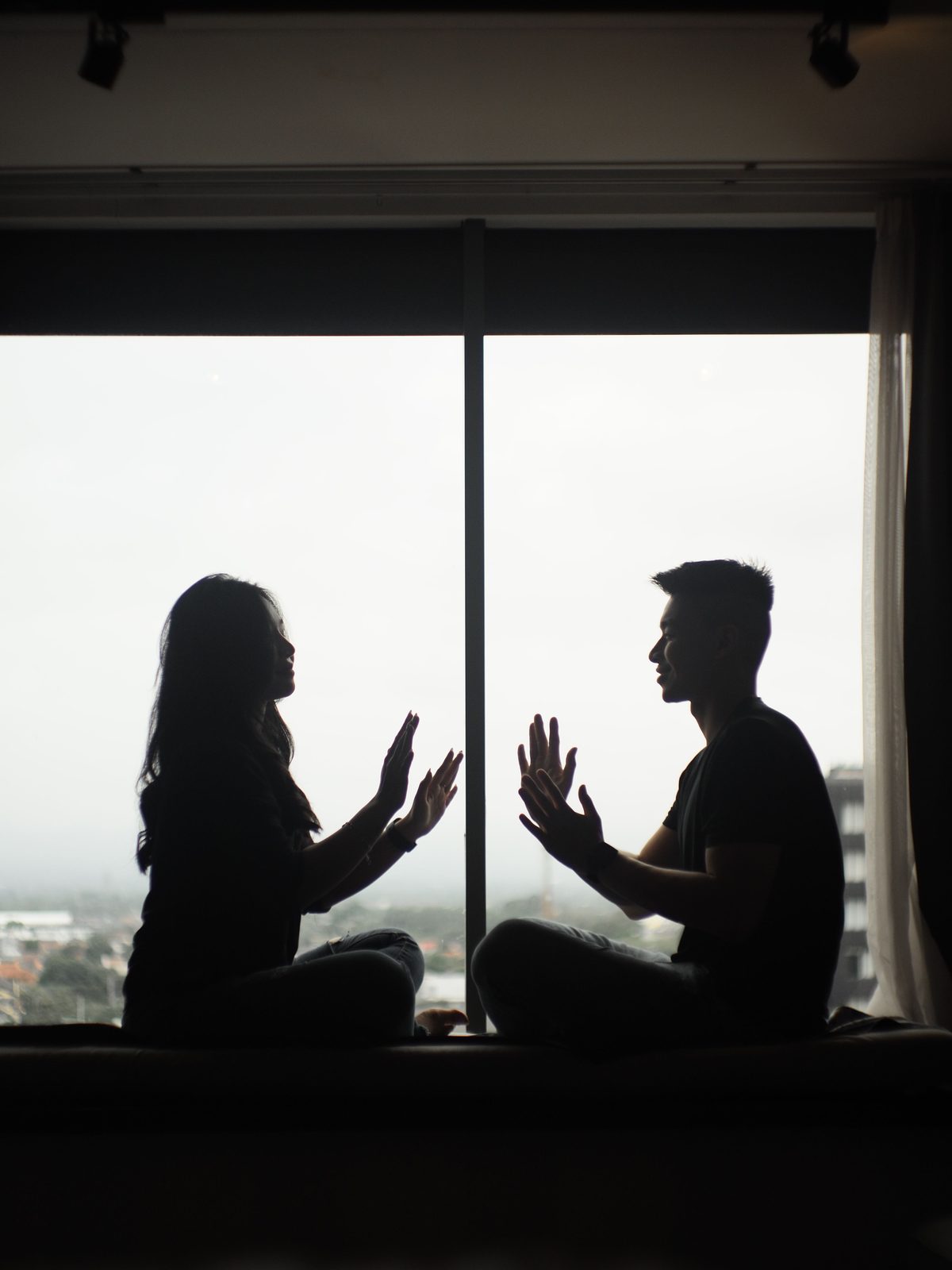 Two people sitting face to face at a window above the city