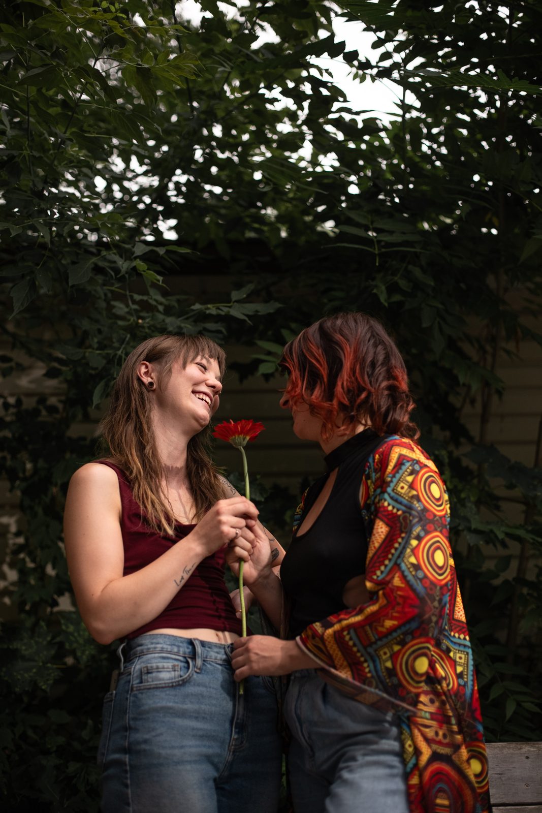 Isa and El facing each other, holding a single red flower between them